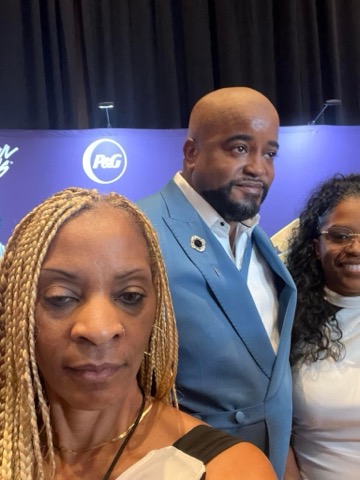 Three people in front of a P&G backdrop — a woman with long blonde braids and a nose ring, a bald man with a beard in a light blue suit jacket, and a woman with curly dark hair and glasses in a white top