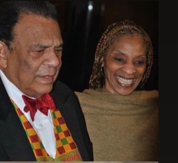 An older gentleman in a colorful checkered vest and red bow tie laughing with a smiling woman with braided hair, both looking down toward each other