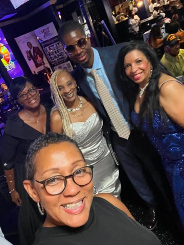 Five well-dressed people together at an evening event, in front of a backdrop for Jazz in the Garden
