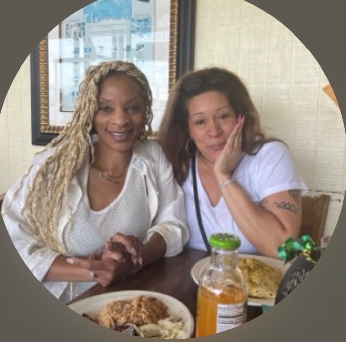 Two smiling women together at a restaurant table, plates of food between them