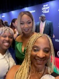 Three smiling women together at an event, one in a green top, a blue DREAM backdrop behind them