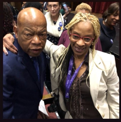 A close photograph of two people smiling together at a crowded professional event, a congressional lanyard at the woman’s neck and red curtains behind them