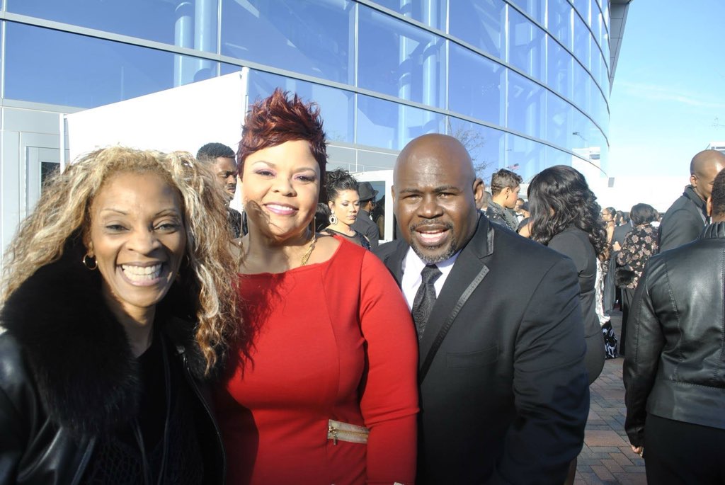 Three smiling people together outdoors in front of a modern building of blue glass