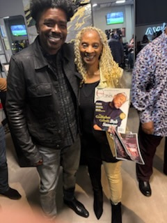 A man in a black leather jacket beside a smiling woman in a black top and gold trousers, holding up two publications, one carrying a JET magazine cover