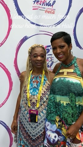 Two smiling women together at the Essence Festival, the New Orleans and Coca-Cola backdrop behind them